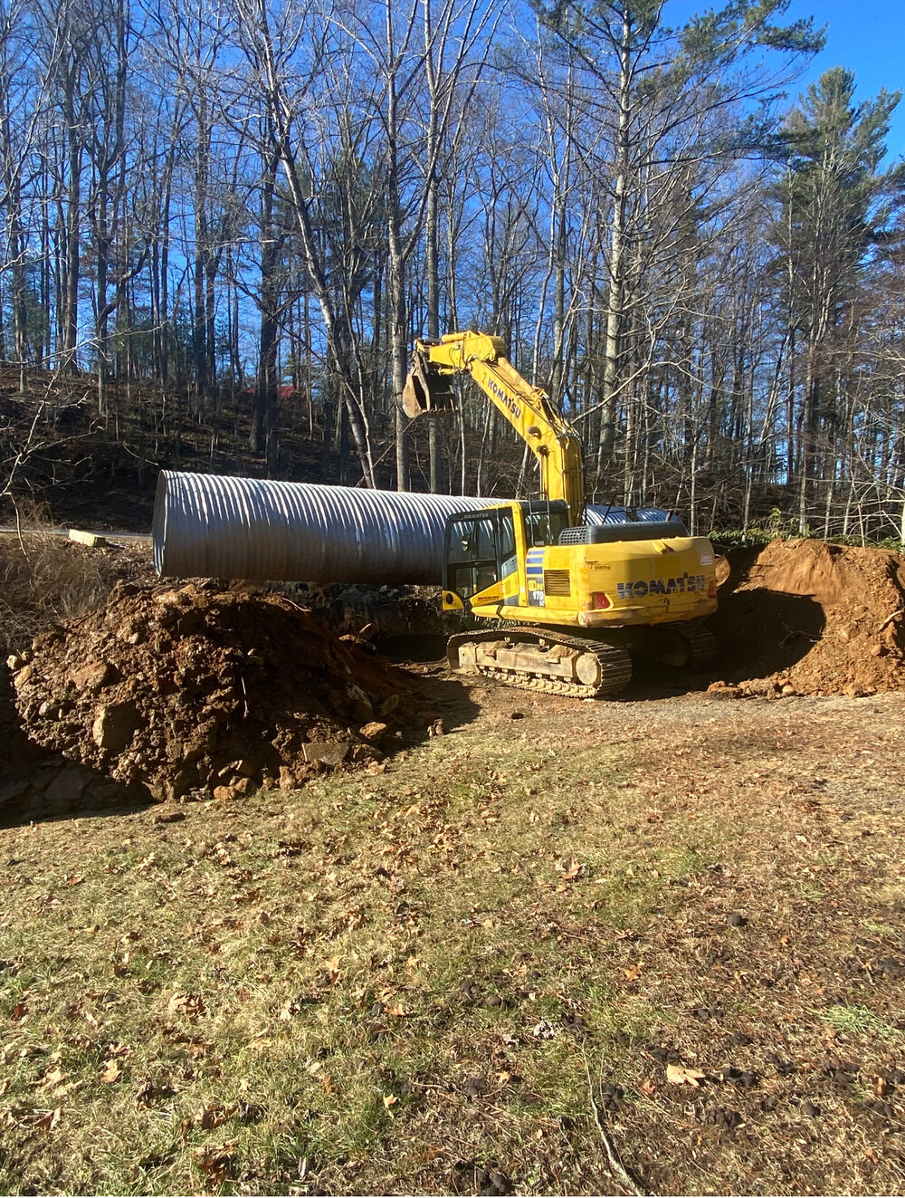 An excavator setting large culvert pipe on a hillside under a blue sky
