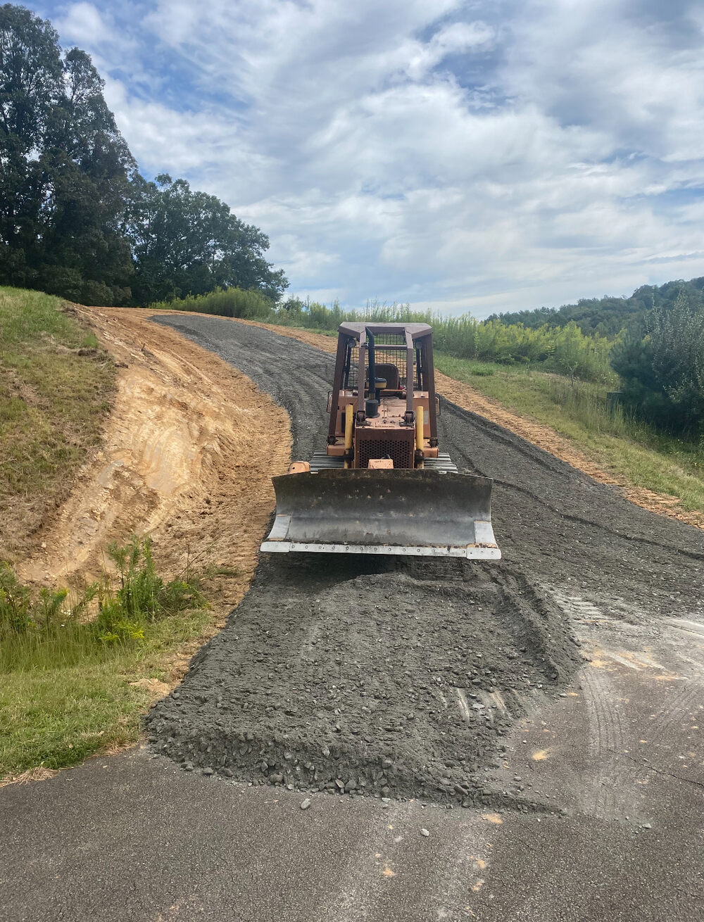 A bulldozer grading a fresh gravel road with a long mountain valley view behind it