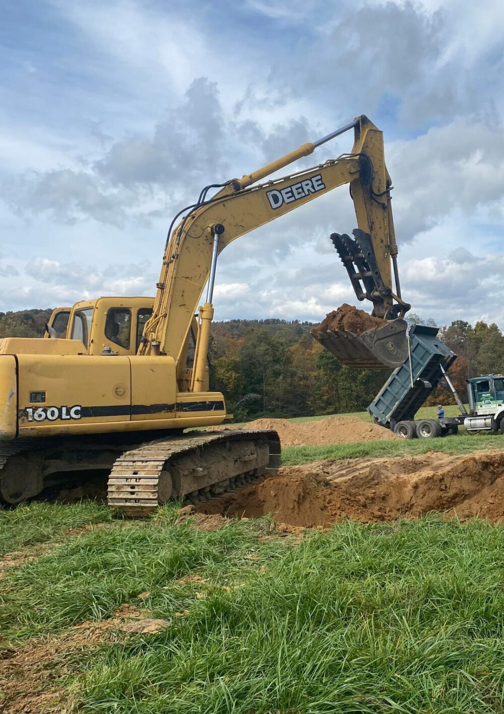 A tracked excavator digging on a green site under a dramatic cloudy sky